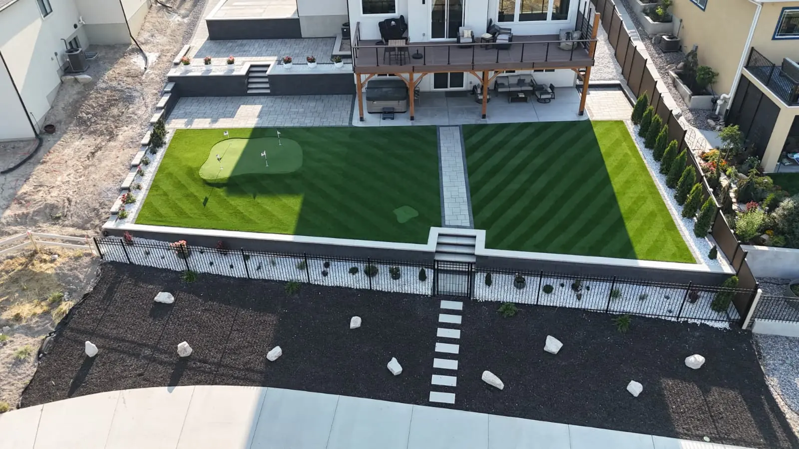 Aerial view of a backyard putting green and striped artificial turf divided by a paver walkway