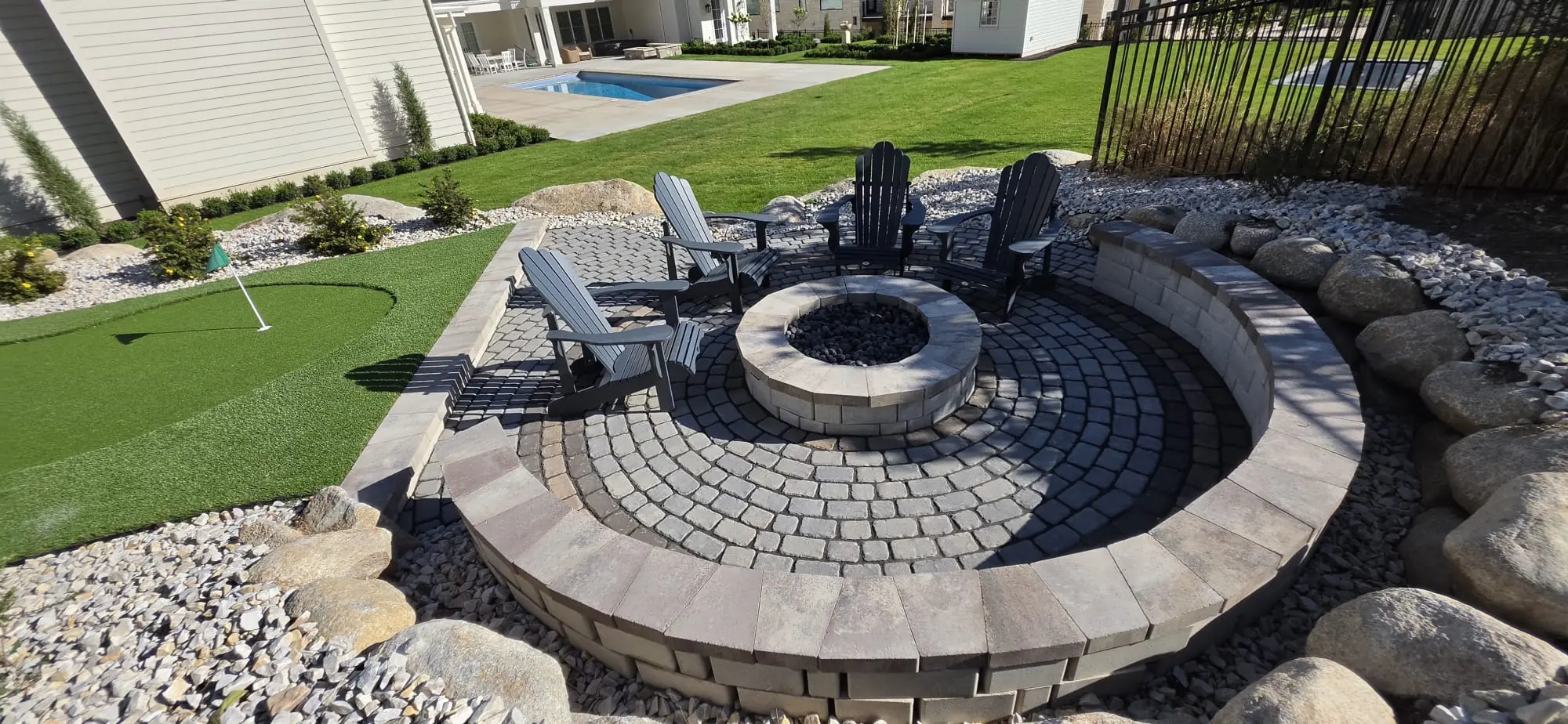 Round stone fire pit on a circular paver patio with chairs and a curved seating wall