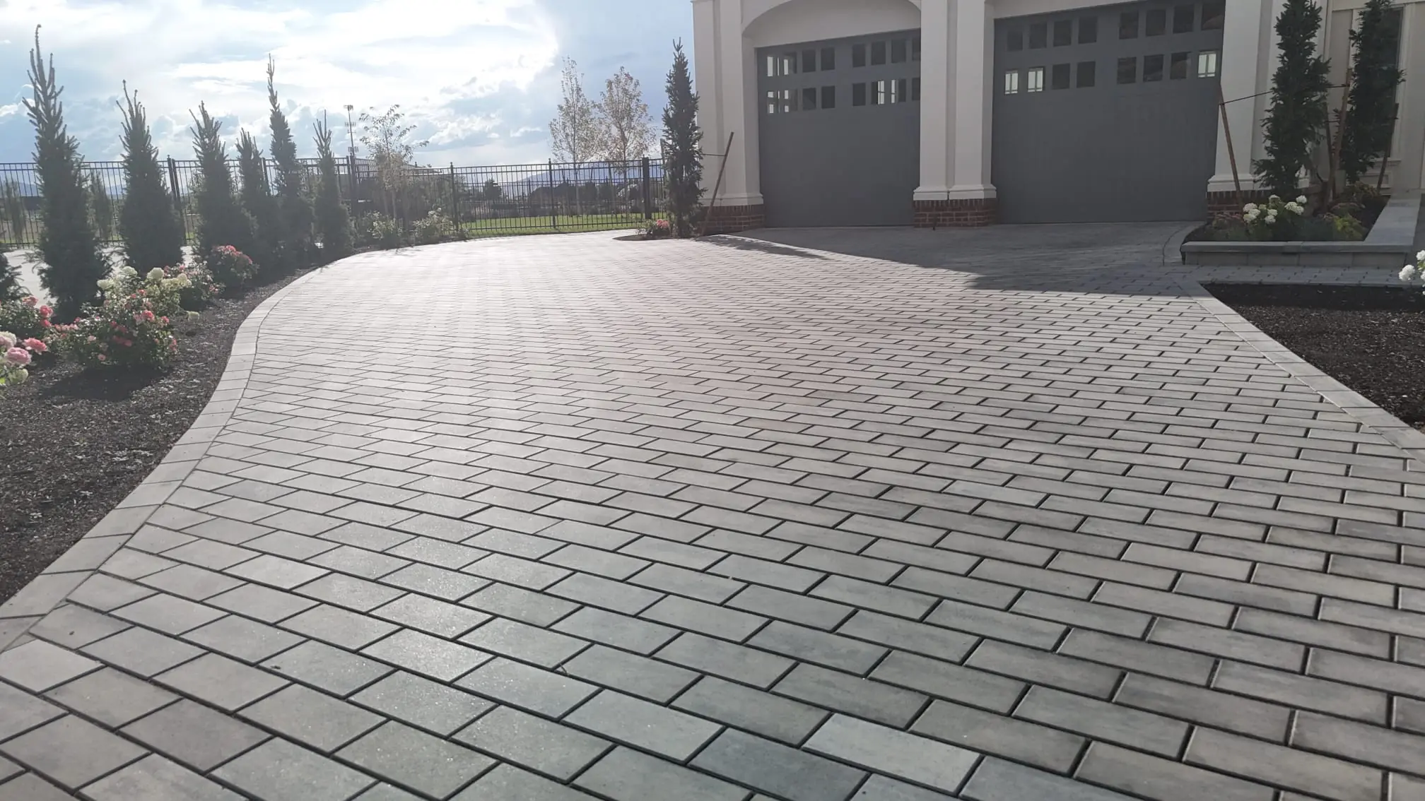 Paver driveway with a curved edge beside a landscaped hillside home