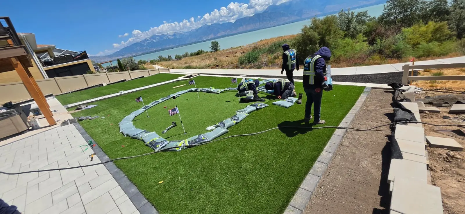Crew installing an artificial turf putting green beside a paver patio with lake views