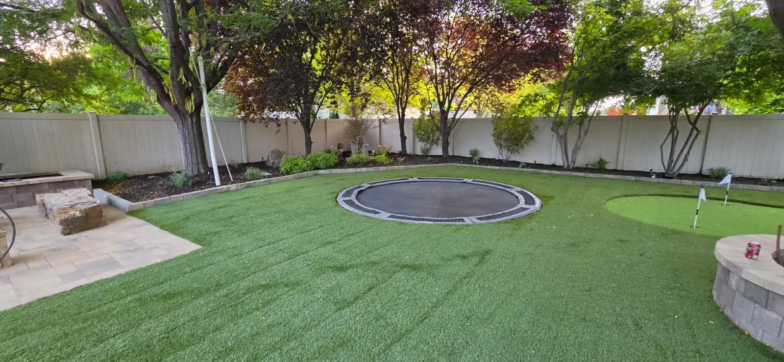 Round in-ground trampoline in artificial turf beside a backyard putting green and patio