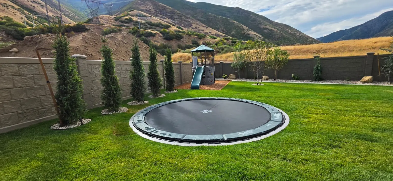 Round in-ground trampoline in a lawn beside a playset with mountain views
