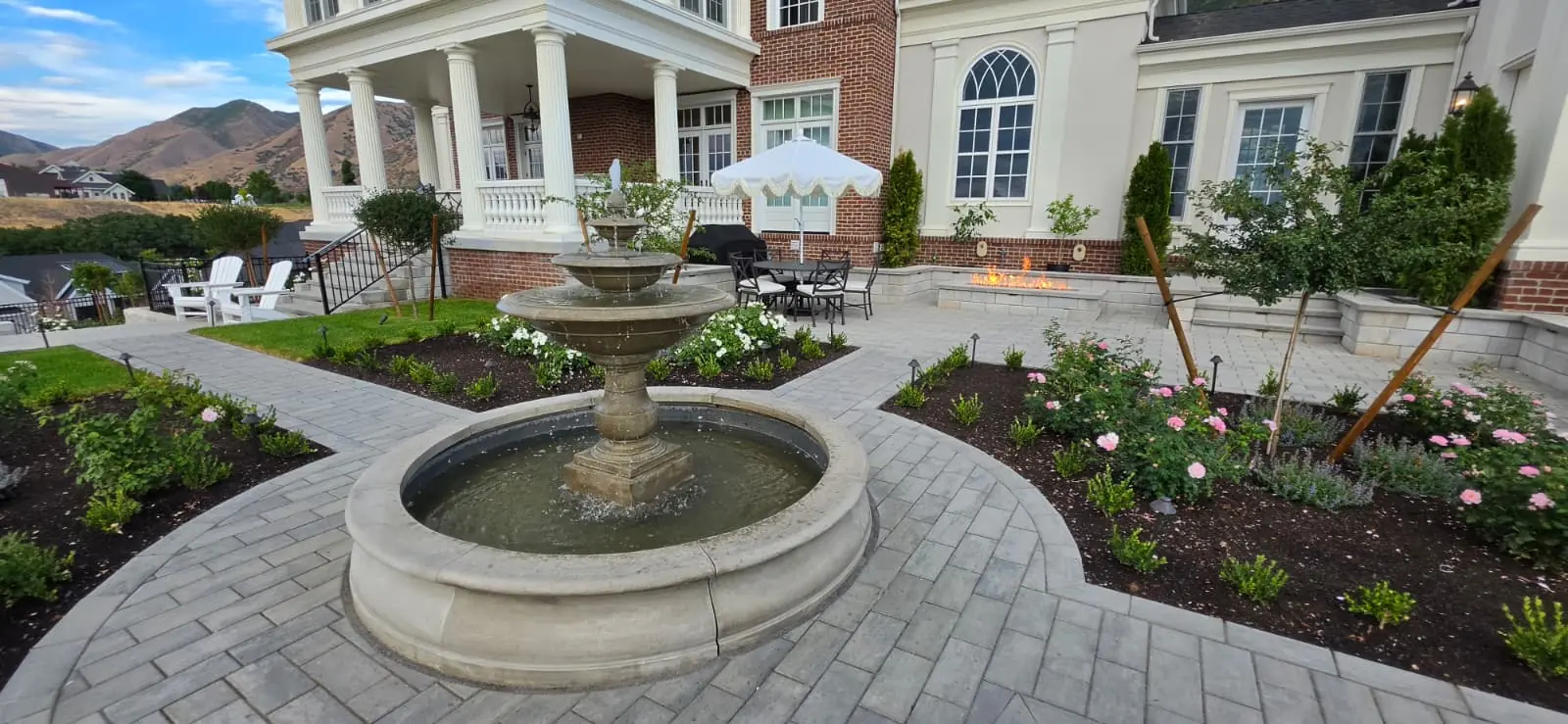 Tiered fountain in a circular basin surrounded by a paver patio and flower beds