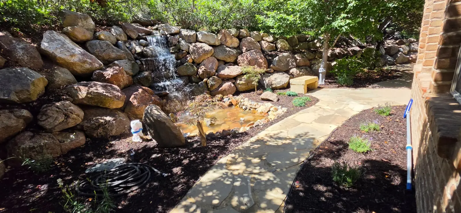 Natural rock waterfall flowing into a small pond beside a stone walkway